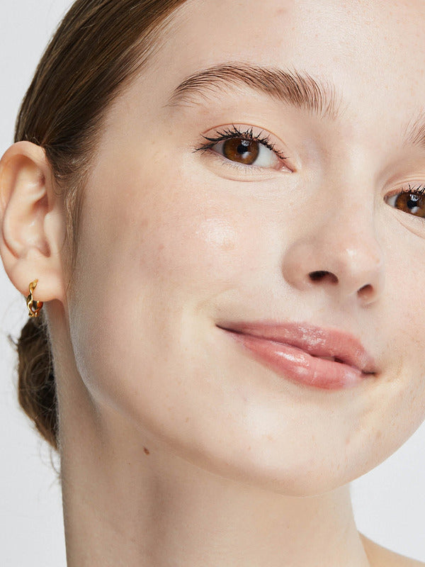 Close-up portrait of a woman wearing Ere Perez Oat Milk Foundation in Nougat, with an even light-beige complexion, faint freckles across her cheeks and softly glossy pink lips.