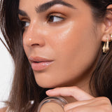 Model wearing Ere Perez Vanilla Highlighter Balm and holding the open product