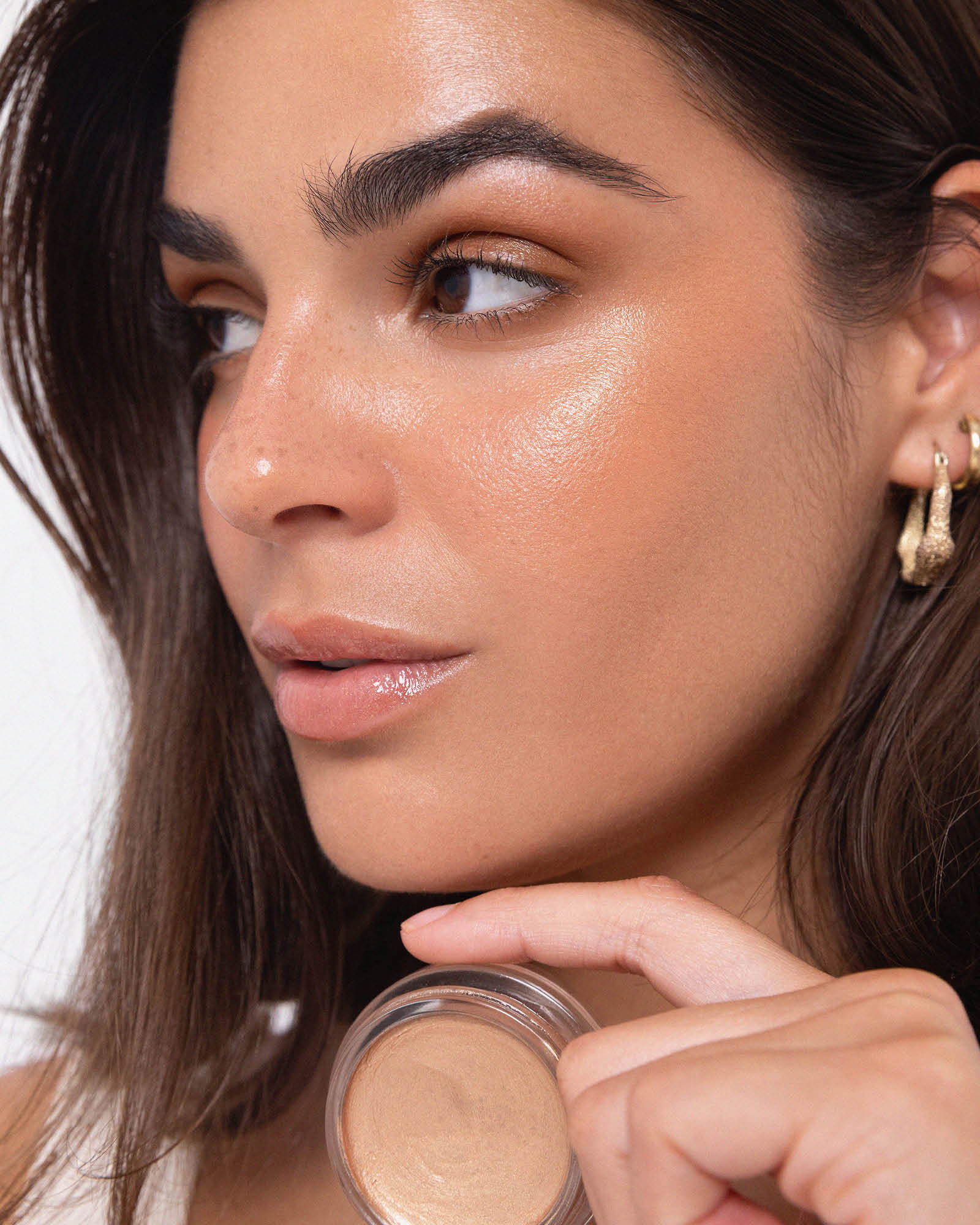 Model wearing Ere Perez Vanilla Highlighter Balm and holding the open product