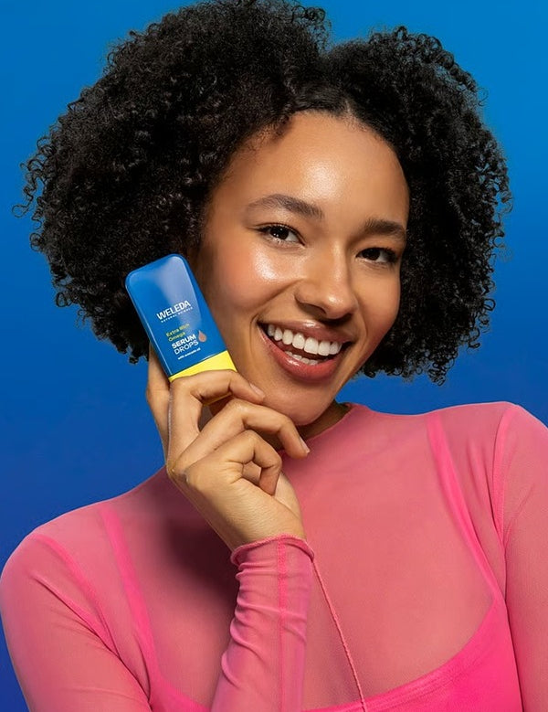 Model holding Weleda Extra Rich Omega Serum Booster Drops beside nourished glowing skin