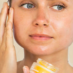 Woman with a nose ring smoothing Ere Perez Papaya SOS Marmalade onto her cheek while holding the jar