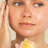 Woman with a nose ring smoothing Ere Perez Papaya SOS Marmalade onto her cheek while holding the jar