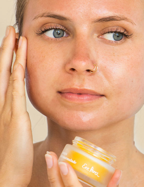 Woman with a nose ring smoothing Ere Perez Papaya SOS Marmalade onto her cheek while holding the jar