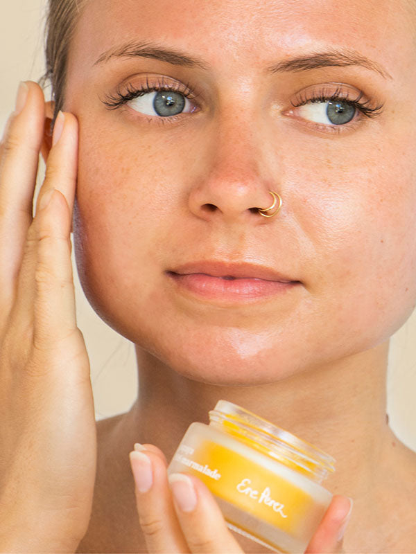 Woman with a nose ring smoothing Ere Perez Papaya SOS Marmalade onto her cheek while holding the jar