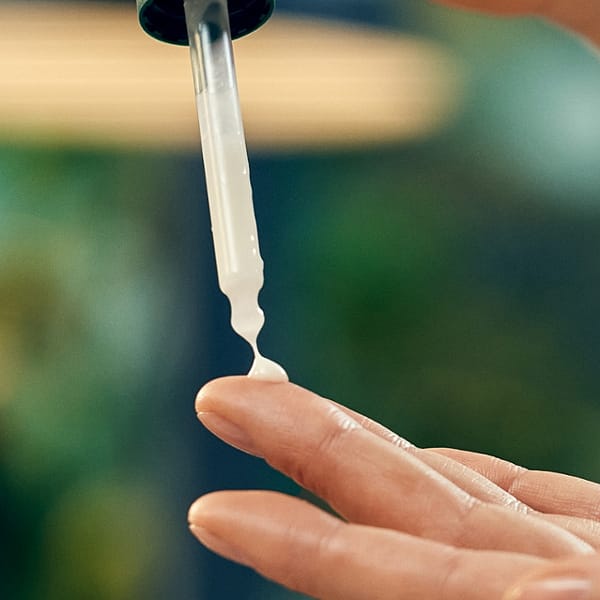 Firming face serum pipette being squeezed onto a finger before application.