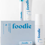Vanessa Megan Foodie Blue Raspberry four-piece Body Bundle: foaming body wash, body moisturiser, face and body mist, and lip balm arranged around the blue gift box on a pale stone surface.