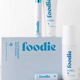 Vanessa Megan Foodie Blue Raspberry four-piece Body Bundle: foaming body wash, body moisturiser, face and body mist, and lip balm arranged around the blue gift box on a pale stone surface.