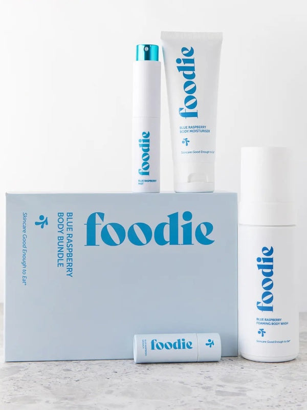 Vanessa Megan Foodie Blue Raspberry four-piece Body Bundle: foaming body wash, body moisturiser, face and body mist, and lip balm arranged around the blue gift box on a pale stone surface.