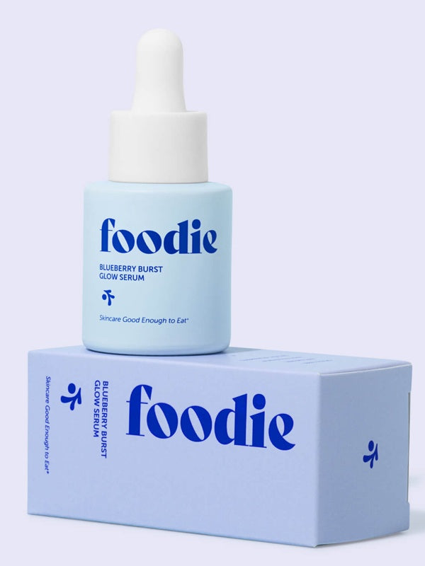 Vanessa Megan Foodie Blueberry Burst Glow Serum 20ml blue dropper bottle standing on its matching lilac carton against a lilac background.