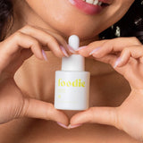 Vanessa Megan Foodie Lemon Aid Pimple Gel 20ml held beneath a smiling model's chin, with her fingers forming a heart around the yellow-labelled dropper bottle.