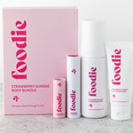 Vanessa Megan Foodie Strawberry Sundae four-piece Body Bundle: foaming body wash, body moisturiser, face and body mist, and lip balm standing beside the pink gift box on a pale stone surface.