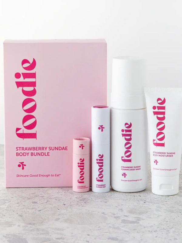 Vanessa Megan Foodie Strawberry Sundae four-piece Body Bundle: foaming body wash, body moisturiser, face and body mist, and lip balm standing beside the pink gift box on a pale stone surface.