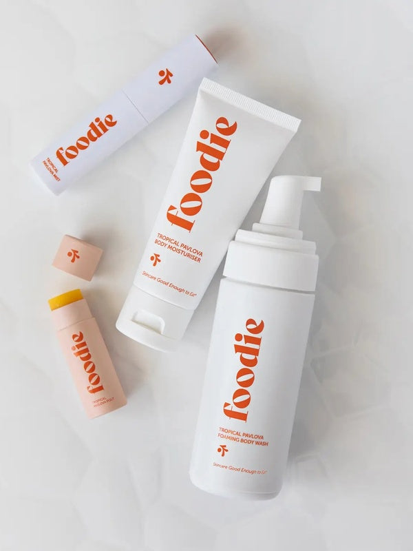Vanessa Megan Foodie Tropical Pavlova four-piece Body Bundle: foaming body wash, body moisturiser, face and body mist, and lip balm arranged on softly folded white fabric, with the lip balm open.