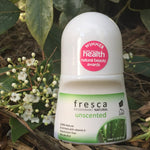 Fresca Unscented natural roll-on deodorant bottle standing among green leaves and small white flowers in an outdoor botanical setting.
