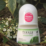 Fresca Unscented natural roll-on deodorant bottle standing among green leaves and small white flowers in an outdoor botanical setting.