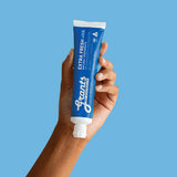 A hand holding a blue Grants Extra Fresh +HA 110g toothpaste tube against a blue background.