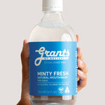 Hand holding a bottle of Grants Minty Fresh Herbal Mouthwash against a pale background.