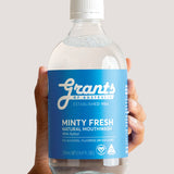 Hand holding a bottle of Grants Minty Fresh Herbal Mouthwash against a pale background.