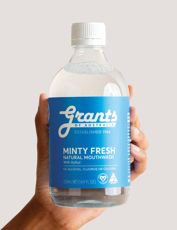 Hand holding a bottle of Grants Minty Fresh Herbal Mouthwash against a pale background.