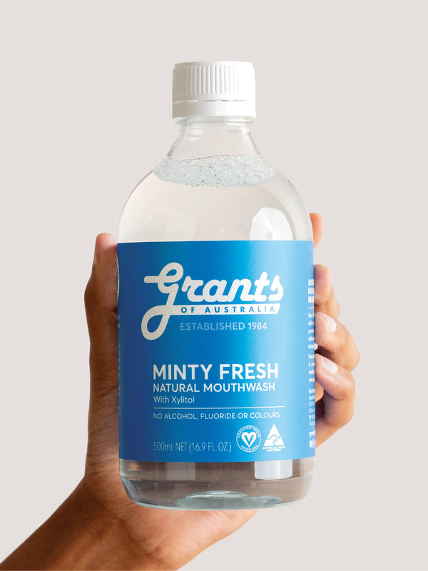 Hand holding a bottle of Grants Minty Fresh Herbal Mouthwash against a pale background.