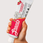 Hand holding a tube of Grants Kids Strawberry Surprise fluoride-free toothpaste against a pale background.