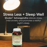Green Nutritionals Shoden Ashwagandha bottle on a wooden bedside table beneath a glowing reading lamp, beside a dark mug and bed pillows. Overlaid text reads Stress Less + Sleep Well and promotes stress relief and restful sleep.