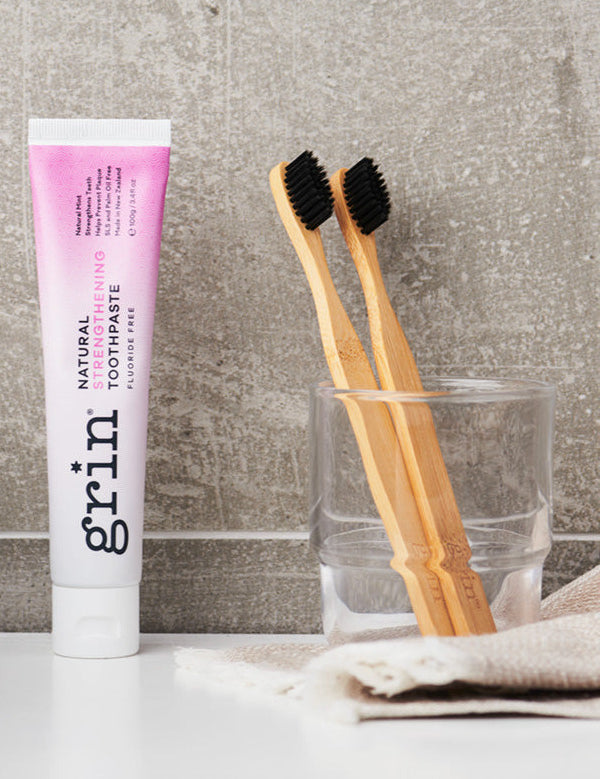Grin Strengthening Toothpaste with bamboo toothbrushes in a bathroom