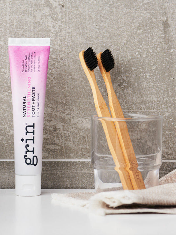 Grin Strengthening Toothpaste with bamboo toothbrushes in a bathroom