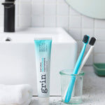Grin Freshening Toothpaste with toothbrushes by a bathroom sink