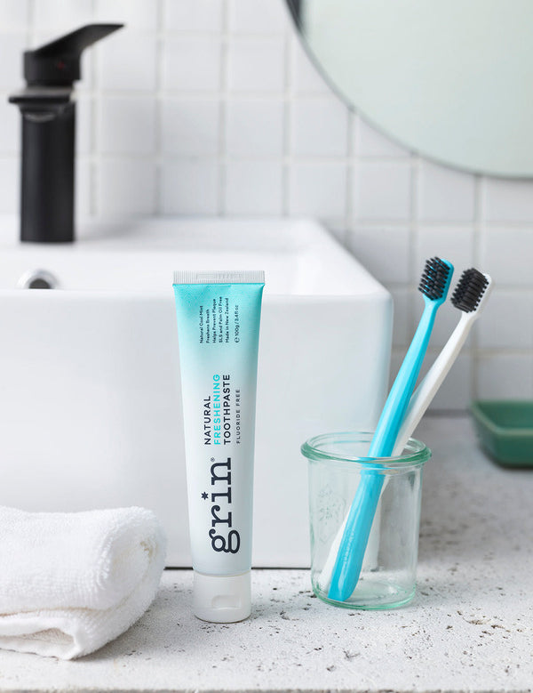 Grin Freshening Toothpaste with toothbrushes by a bathroom sink