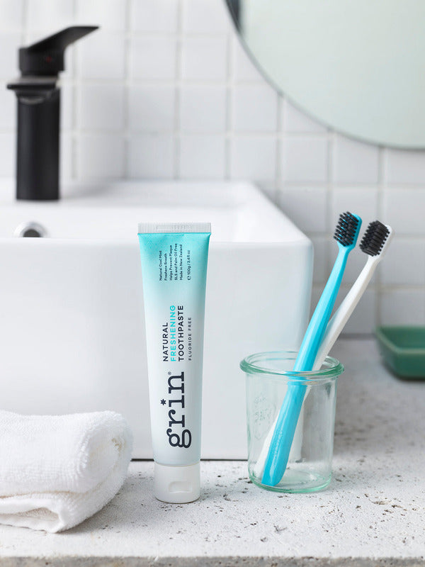 Grin Freshening Toothpaste with toothbrushes by a bathroom sink