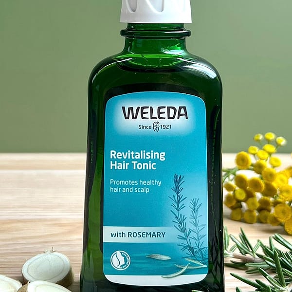 Revitalising Hair Tonic bottle on a sage green background with its ingredients rosemary leaves and horseradish root.