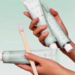 Hands holding Davids Peppermint Toothpaste tubes with a bamboo toothbrush