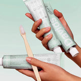 Hands holding Davids Peppermint Toothpaste tubes with a bamboo toothbrush