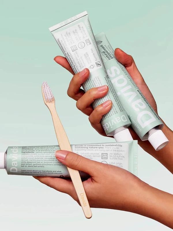 Hands holding Davids Peppermint Toothpaste tubes with a bamboo toothbrush