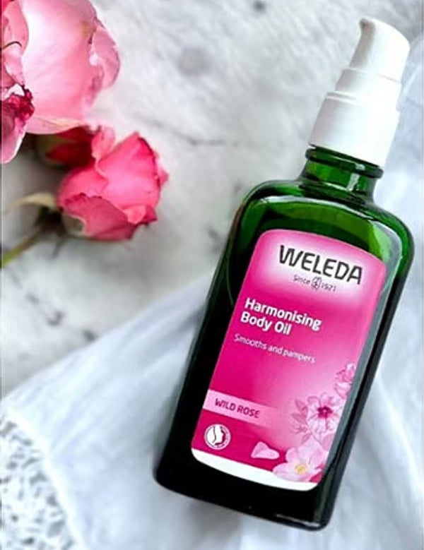 Weleda Harmonising Wild Rose Body Oil styled beside pink roses
