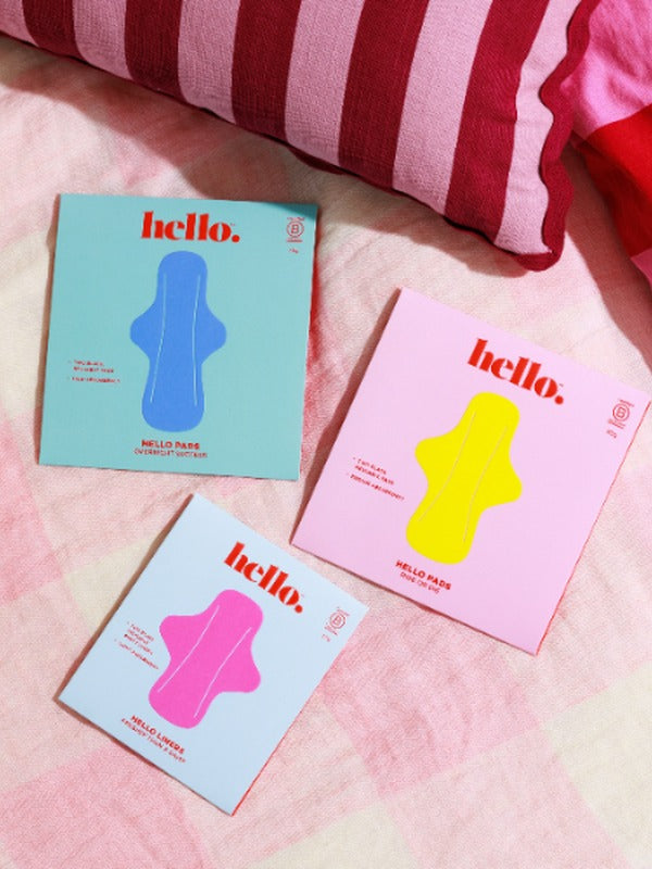 Hello Period liner and pad packaging styled on a bed
