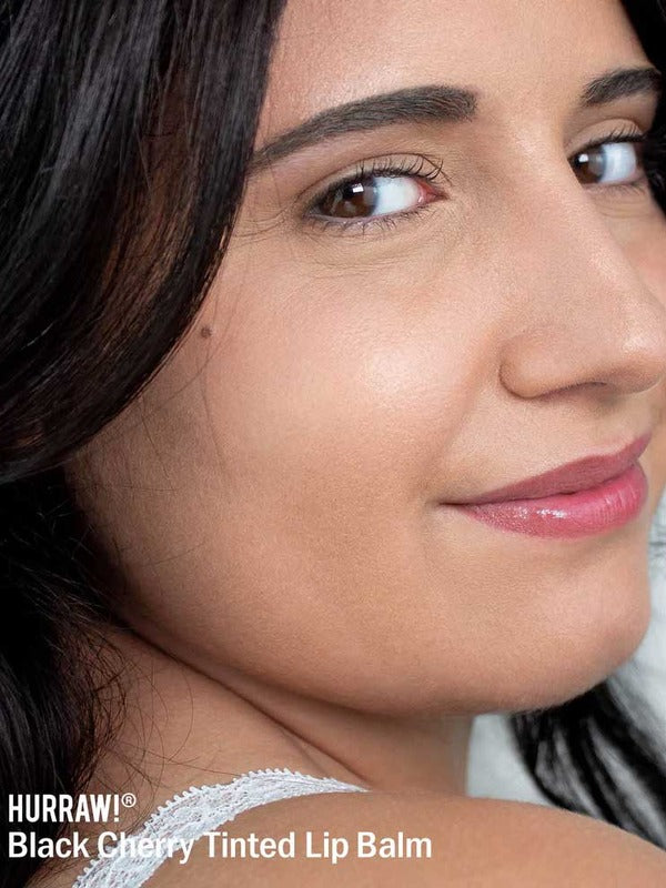 Woman wearing a glossy black-cherry lip tint, with the caption Hurraw Black Cherry Tinted Lip Balm kept visible at the lower edge.