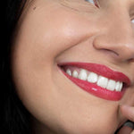 A smiling woman with smooth skin and bright white teeth wears vibrant red Hurraw! Rouge à Lèvres Plantcolor No 1 (4.8g) lipstick. “Hurraw! Rouge à Lèvres Plantcolor No 1” appears in the lower left, highlighting this plant-based lip colour.