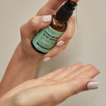 One hand holds an amber Hyaluronic Acid Serum bottle with a mint-green label, with a finger on the black pump above the other open palm.