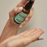One hand holds an amber Hyaluronic Acid Serum bottle with a mint-green label, with a finger on the black pump above the other open palm.