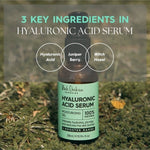 A Hyaluronic Acid Serum bottle rests on grass beneath the heading 3 Key Ingredients. Three labelled circles name hyaluronic acid, juniper berry and witch hazel.