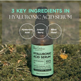 A Hyaluronic Acid Serum bottle rests on grass beneath the heading 3 Key Ingredients. Three labelled circles name hyaluronic acid, juniper berry and witch hazel.