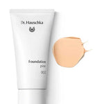 A white tube of Dr Hauschka Foundation 30ml is displayed beside a swatch of light beige cream on a white background; this vegan, natural foundation offers medium coverage.
