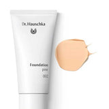 A white tube of Dr Hauschka Foundation 30ml is displayed beside a swatch of light beige cream on a white background; this vegan, natural foundation offers medium coverage.
