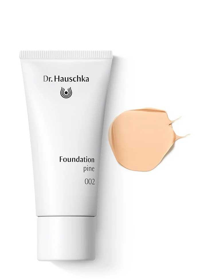 A white tube of Dr Hauschka Foundation 30ml is displayed beside a swatch of light beige cream on a white background; this vegan, natural foundation offers medium coverage.