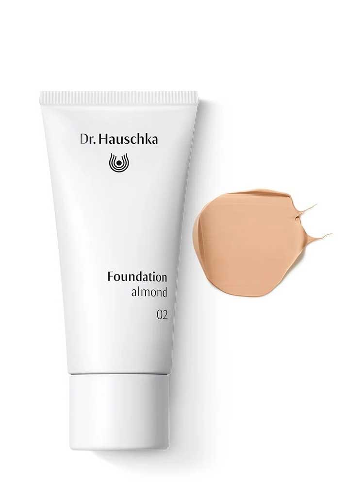 A white tube of Dr Hauschka Foundation 30ml is displayed beside a smear of beige, medium coverage natural foundation on a white background.