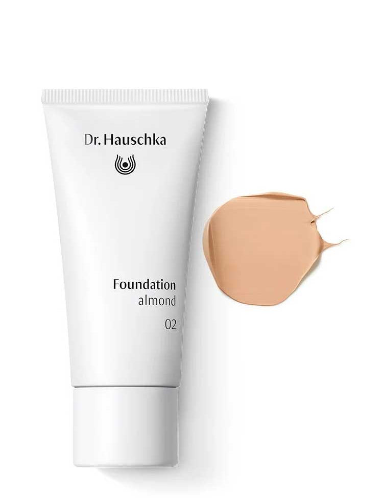A white tube of Dr Hauschka Foundation 30ml is displayed beside a smear of beige, medium coverage natural foundation on a white background.