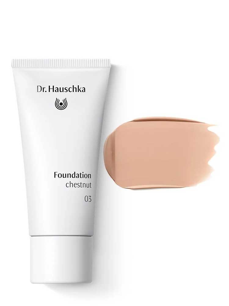 A white tube of Dr Hauschka Foundation 30ml is placed next to a beige natural foundation swatch, both offering medium coverage, on a white background.