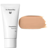 A white tube labeled Dr Hauschka Foundation 30ml stands beside a large swatch of medium coverage, natural foundation in medium beige on a white background.